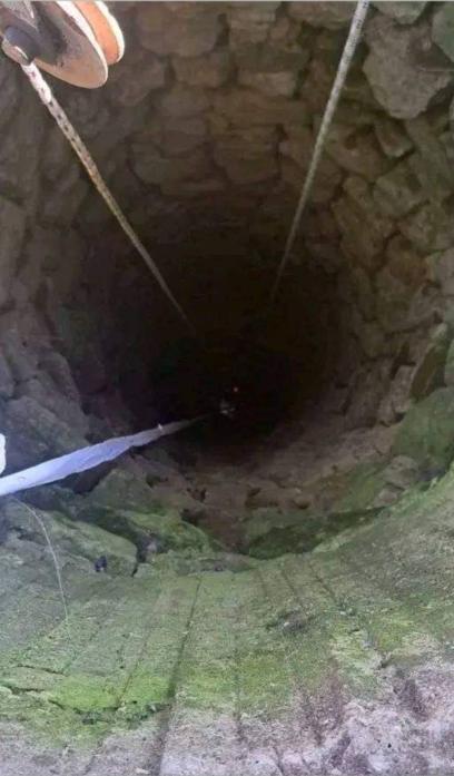 Дълбок кладенец с каменни стени, гледан отгоре; над отвора има макара с верига, а по горните камъни има мъх.